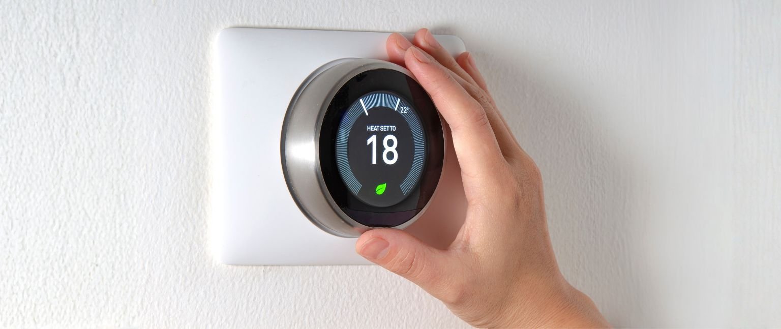 Hand turning on thermostat on white wall.