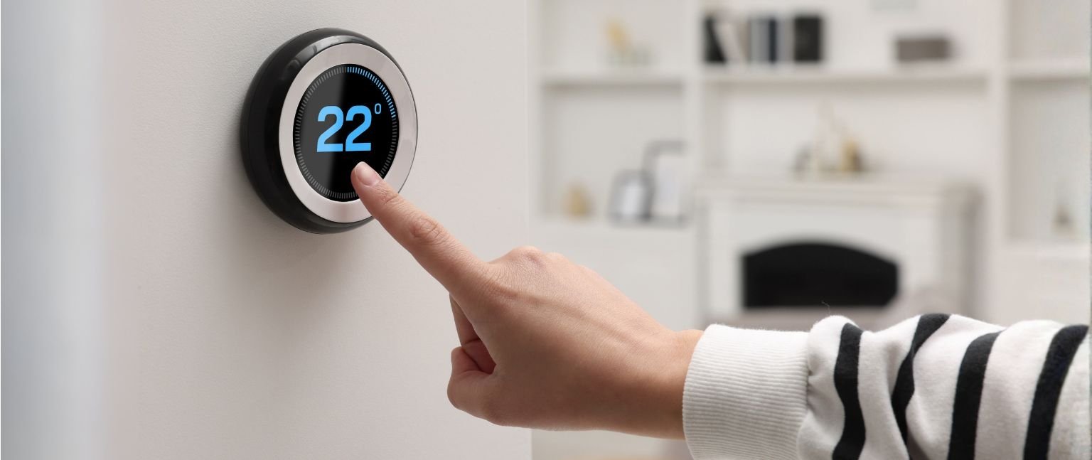 Χέρι ρυθμίζει ψηφιακό smart θερμοστάτη στους 22 βαθμούς σε μοντέρνο καθιστικό